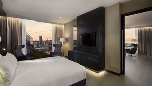 A modern hotel room with a large bed, a flat-screen TV mounted on the wall, and a view of a cityscape through large windows. - Hilton Tallinn Park (Tallinn)
