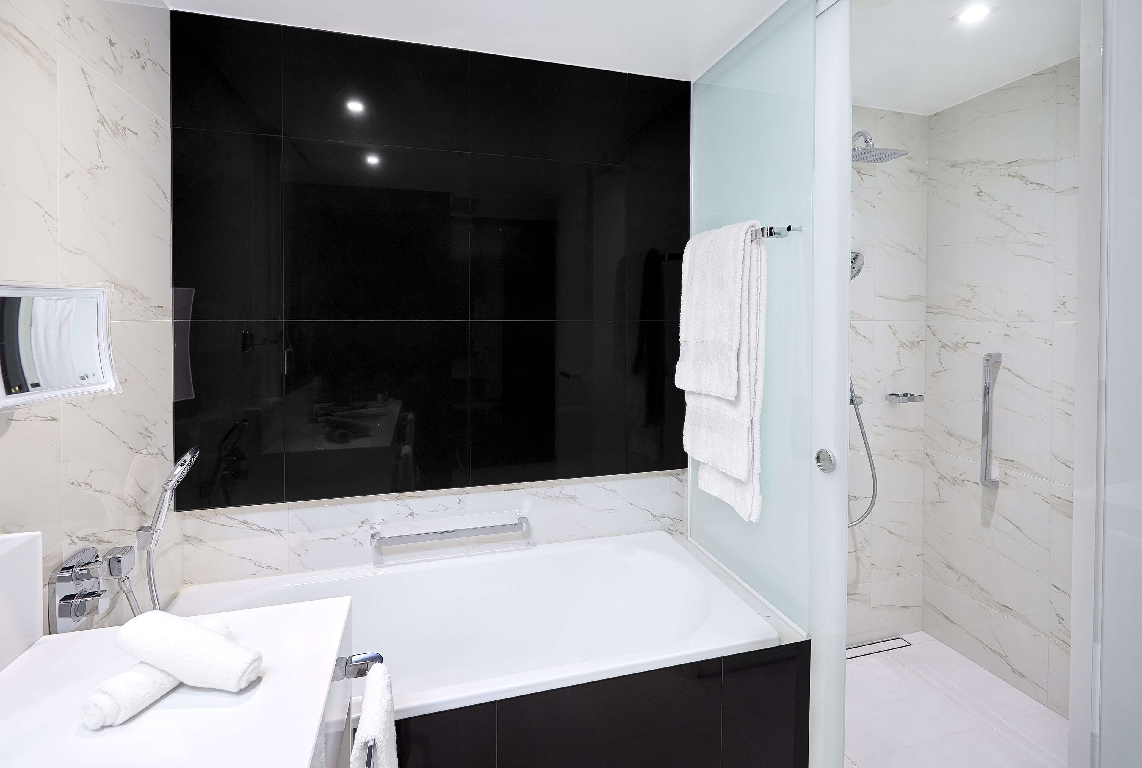 A modern bathroom with a large mirror, a bathtub, a shower area, and marble walls.