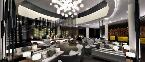 A modern lobby with a central staircase, seating areas, and a large chandelier.