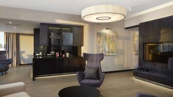 A modern living room with a round black coffee table, a purple armchair, a dark wooden cabinet, and a large flat-screen TV mounted on the wall.