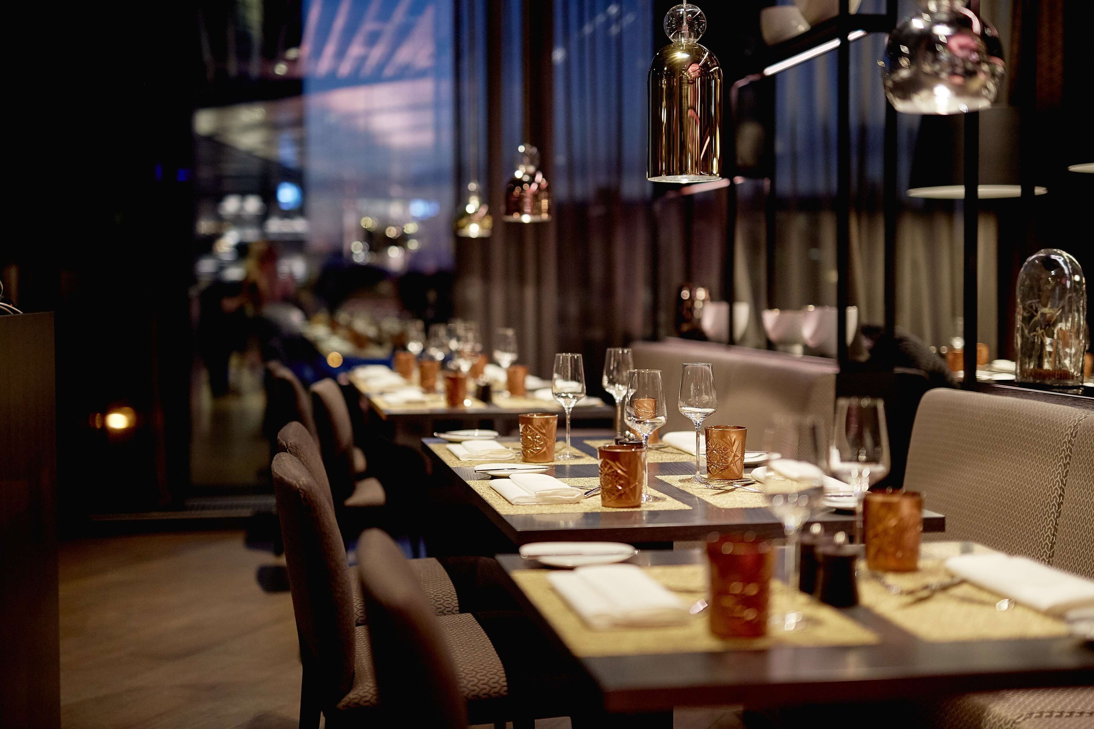 A restaurant with long tables set for dining, featuring elegant table settings and hanging pendant lights.