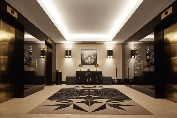 A modern lobby with a geometric patterned carpet, wall-mounted lighting, and a framed artwork above a reception desk. - Hilton Tallinn Park (Tallinn)