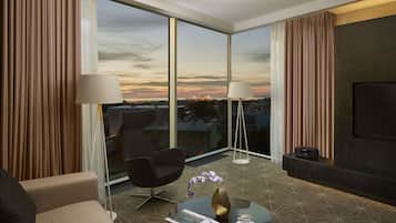 A modern hotel room with a large window, a sofa, a coffee table, and a TV.
