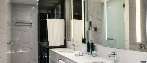 Un baño moderno con ducha envuelta en vidrio, un espejo grande y un tocador doble.