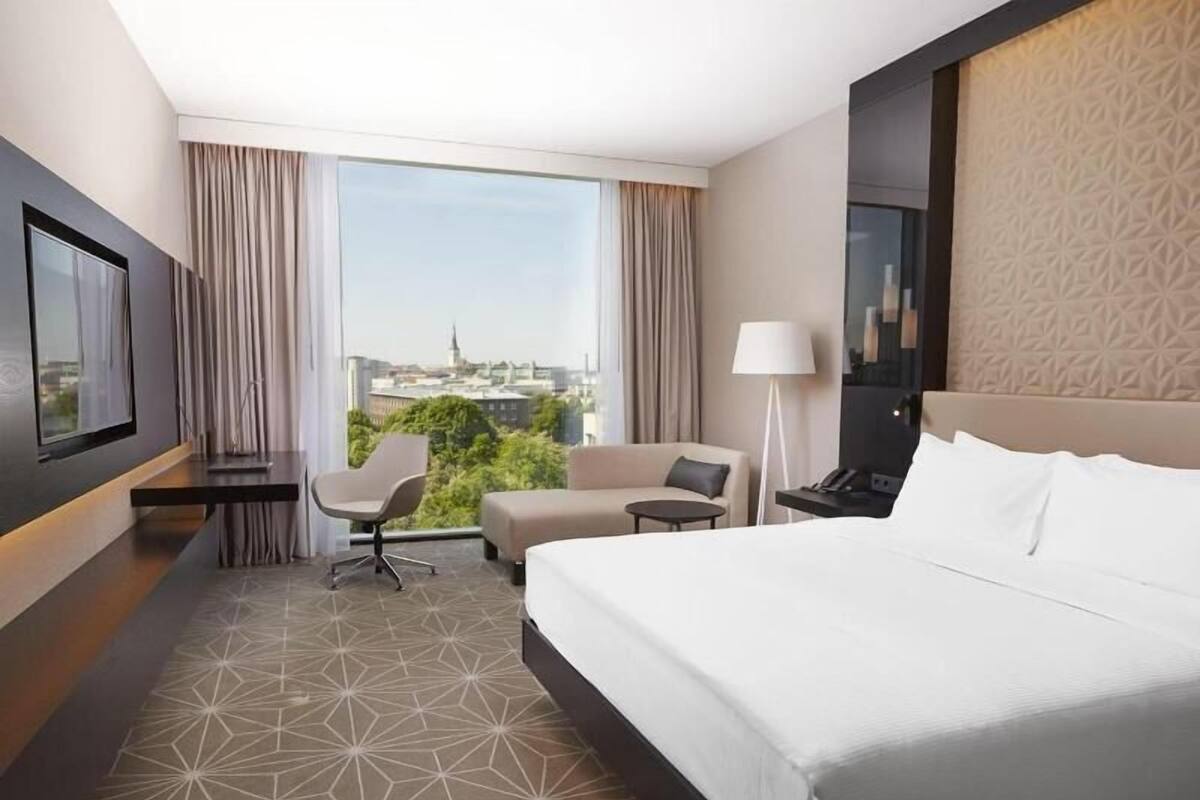 Una camera d'albergo con un letto, una scrivania, una sedia, una lampada e una televisione.