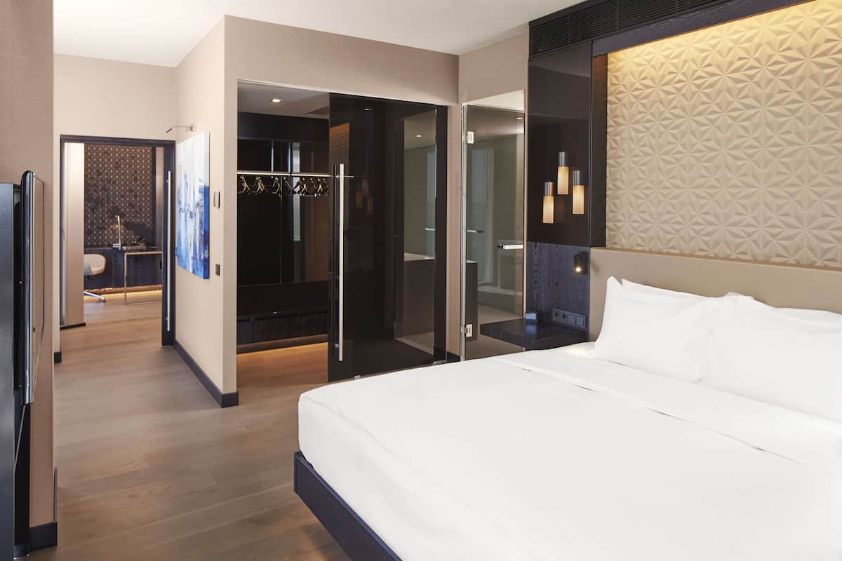 Una moderna camera d'albergo con un letto grande, un armadio a muro e un bagno con doccia in vetro.