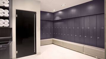 A modern locker room with neatly arranged lockers numbered 1 to 34, a glass door entrance, and a towel rack with folded towels.