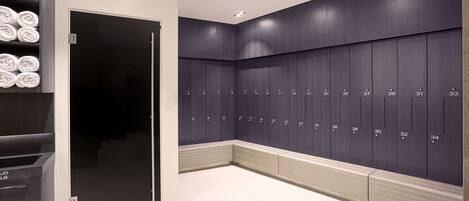 A modern locker room with neatly arranged lockers numbered 1 to 34, a glass door entrance, and a towel rack with folded towels.