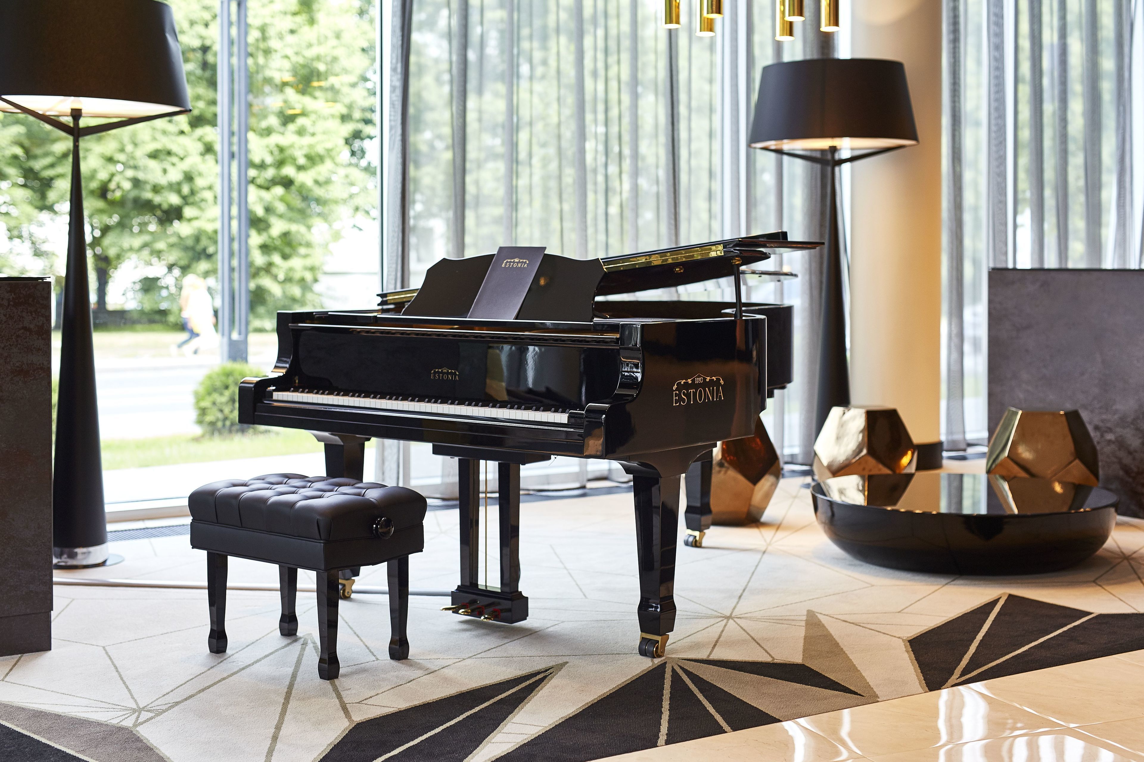 A grand piano in a well-lit room with a modern design, including a geometric patterned rug and contemporary furniture.