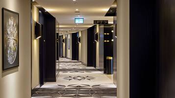 En modern hotellkorridor med ett golv som har ett geometriskt mönster, vägvisningsskyltar och moderna väggmonterade lampor.