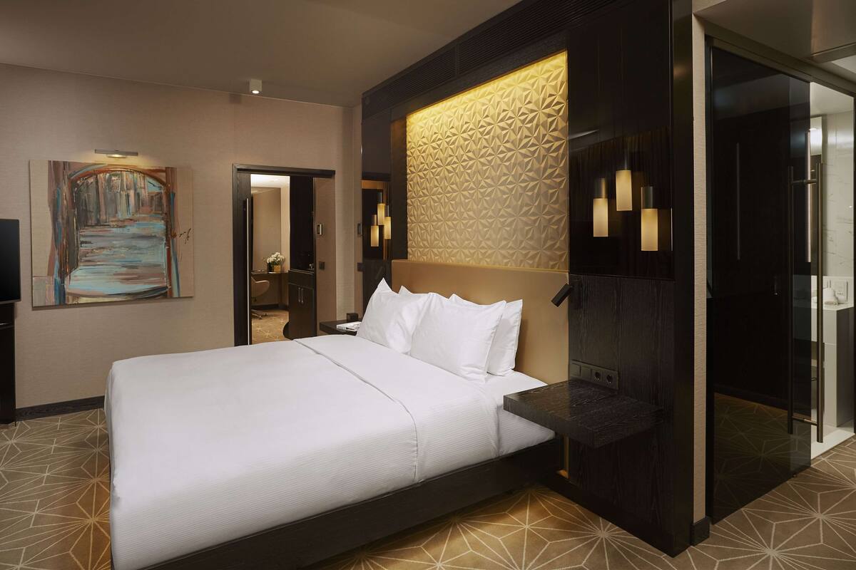 Una camera d'hotel moderna con un letto grande, un box doccia in vetro e una parete con motivo geometrico.