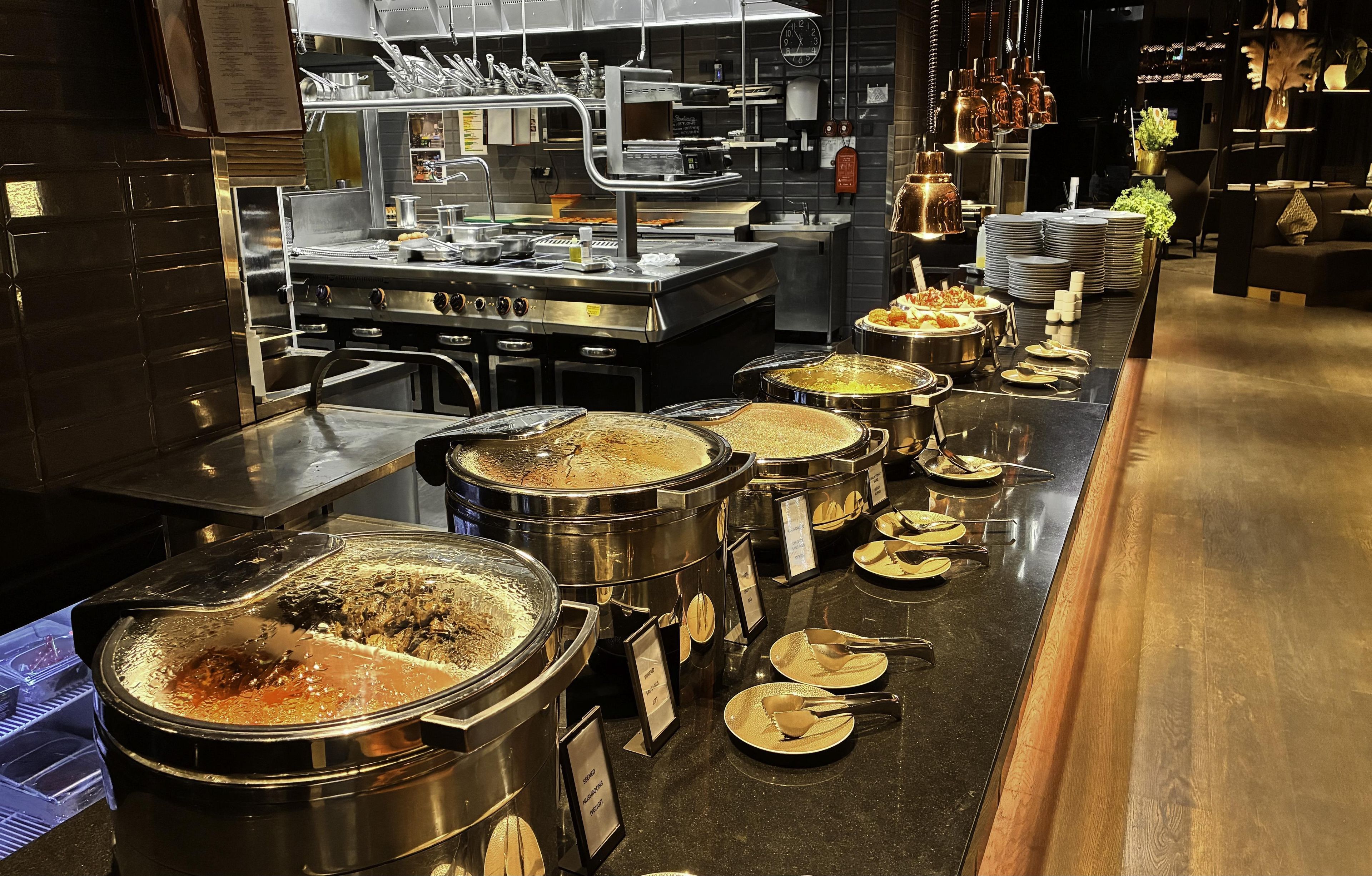 Een buffetopstelling met meerdere aaneenschakelde stations, roestvrijstalen buffetbestek en een gevarieerd assortiment gerechten.