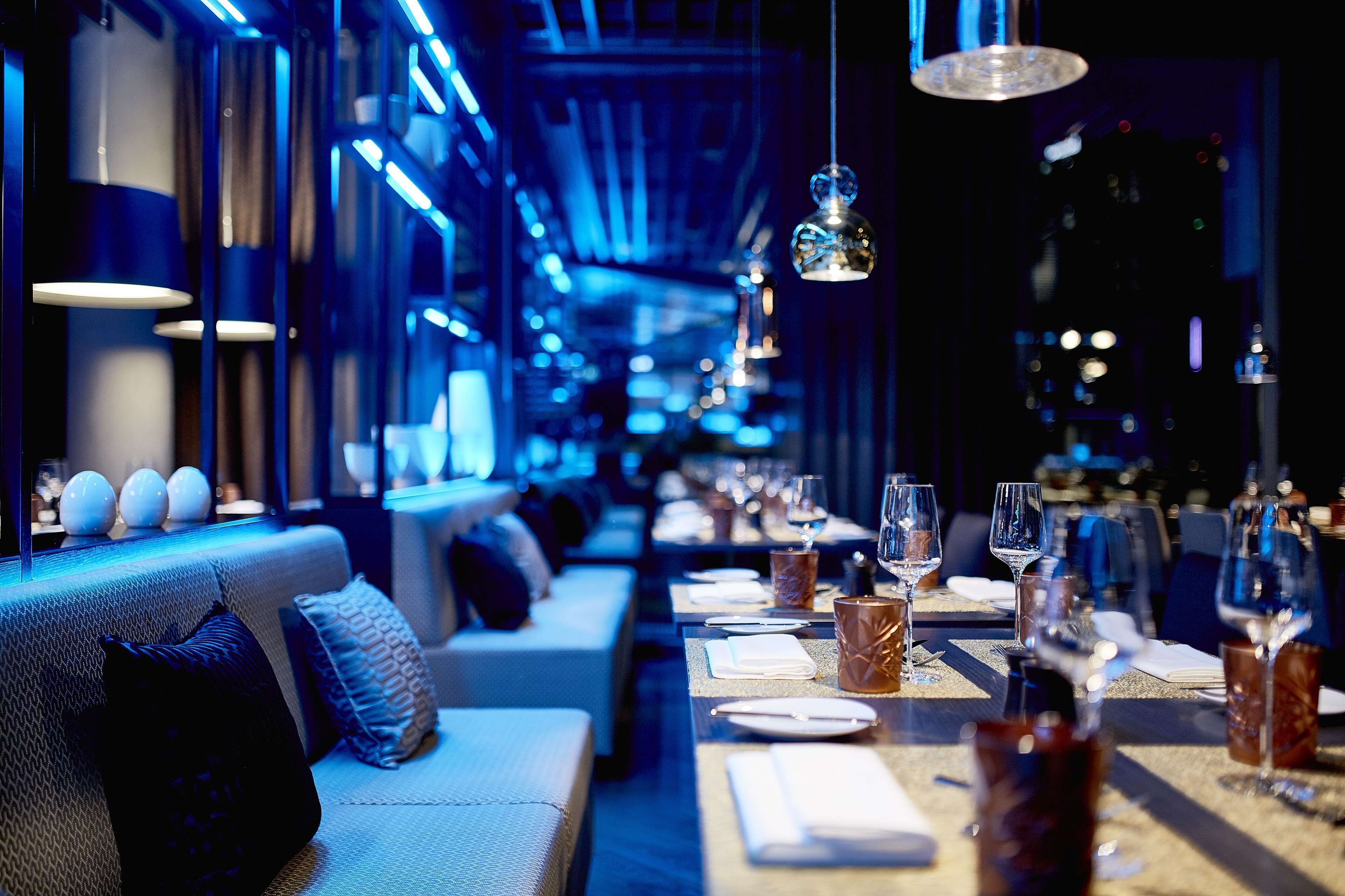 Ein Restaurant mit langen Tischen, blauem stimmungsvollem Licht und modernem Interieur.