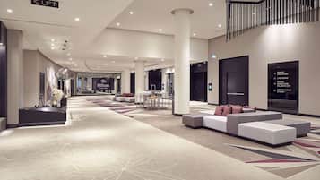 En rummelig hotellobby med et moderne design, med et centralt siddeområde, en receptionsdisk og skilte der viser vej til forskellige områder af hotellet.