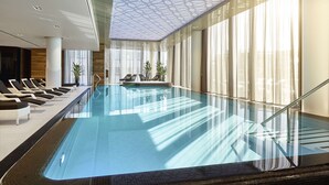 A modern indoor swimming pool with clear glass walls, a geometric ceiling design, and sunlit windows. - Hilton Tallinn Park (Tallinn)