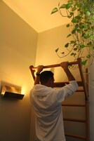 A person using a wooden ladder to reach a plant on a wall.