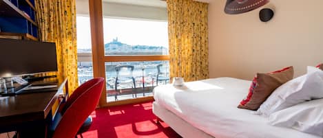 Habitación de hotel con una cama, un escritorio con computadora, una silla y vistas de la ciudad a través de un ventanal grande.