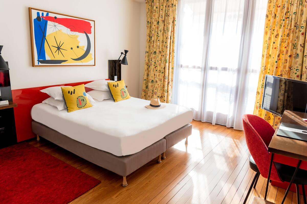 A hotel room with a bed, a desk, a TV, and a window with curtains.