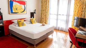 Habitación de hotel con cama, escritorio, televisión y ventana con cortinas.