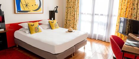 Habitación de hotel con cama, escritorio, televisión y ventana con cortinas.