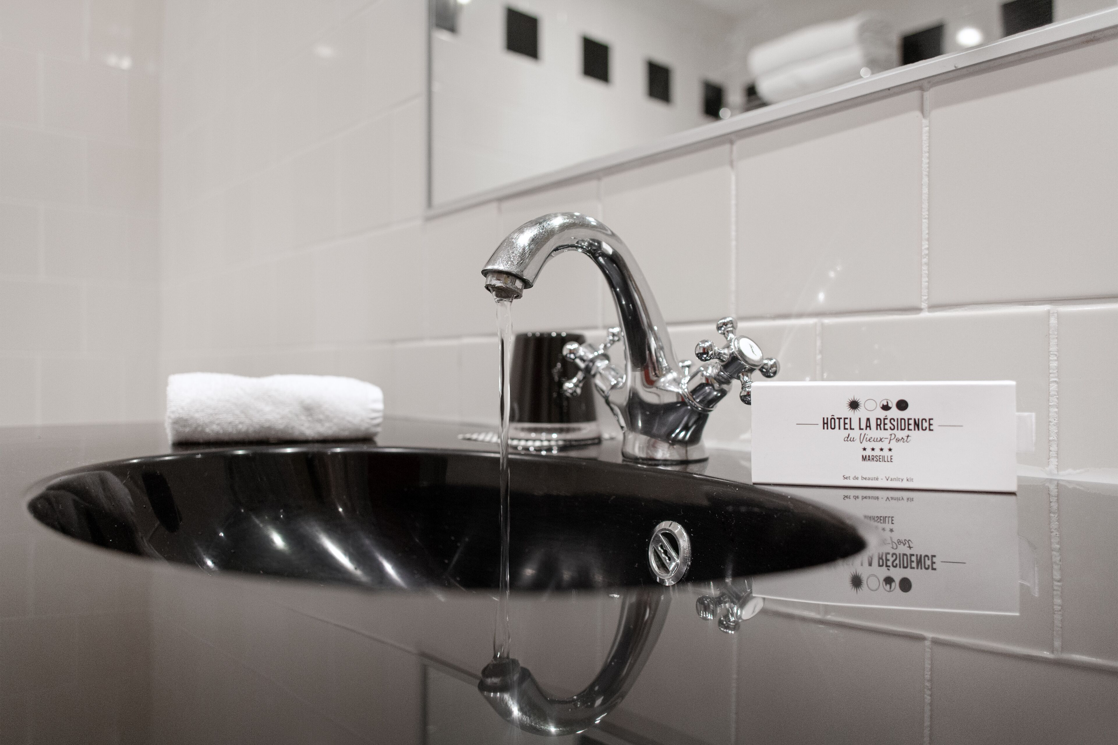 A black sink with a chrome faucet and a white towel. A sign with hotel information is visible.