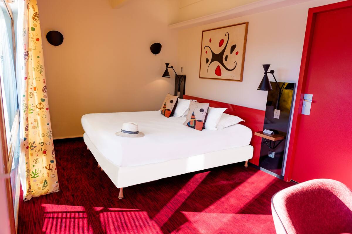 A hotel room with a large bed, a red wall, and a red chair.