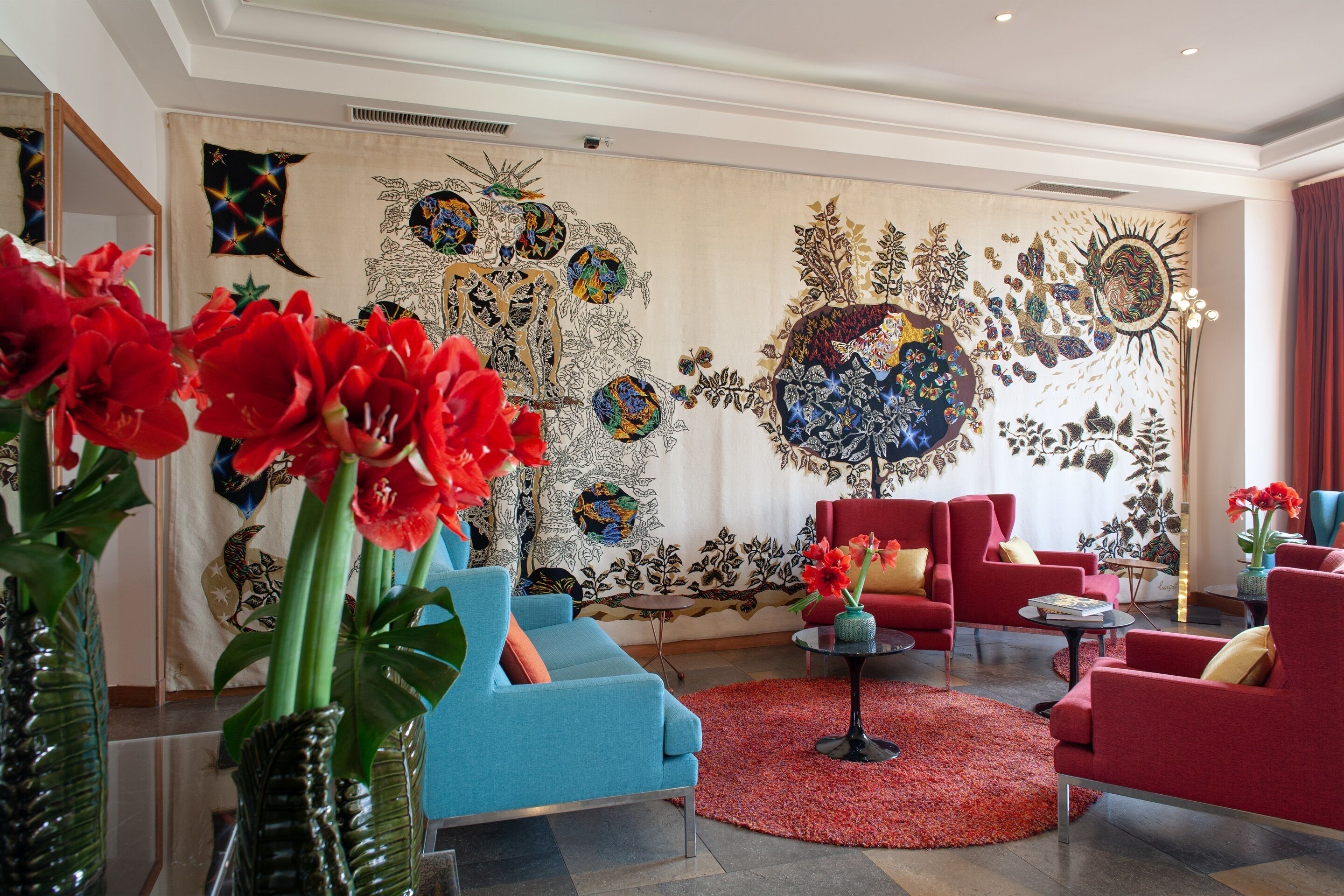 Un salon moderne avec un canapé bleu, des fauteuils rouges et un tapis rouge.