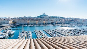 A marina with numerous boats docked, a prominent hill with a tower in the background, and a clear blue sky.
