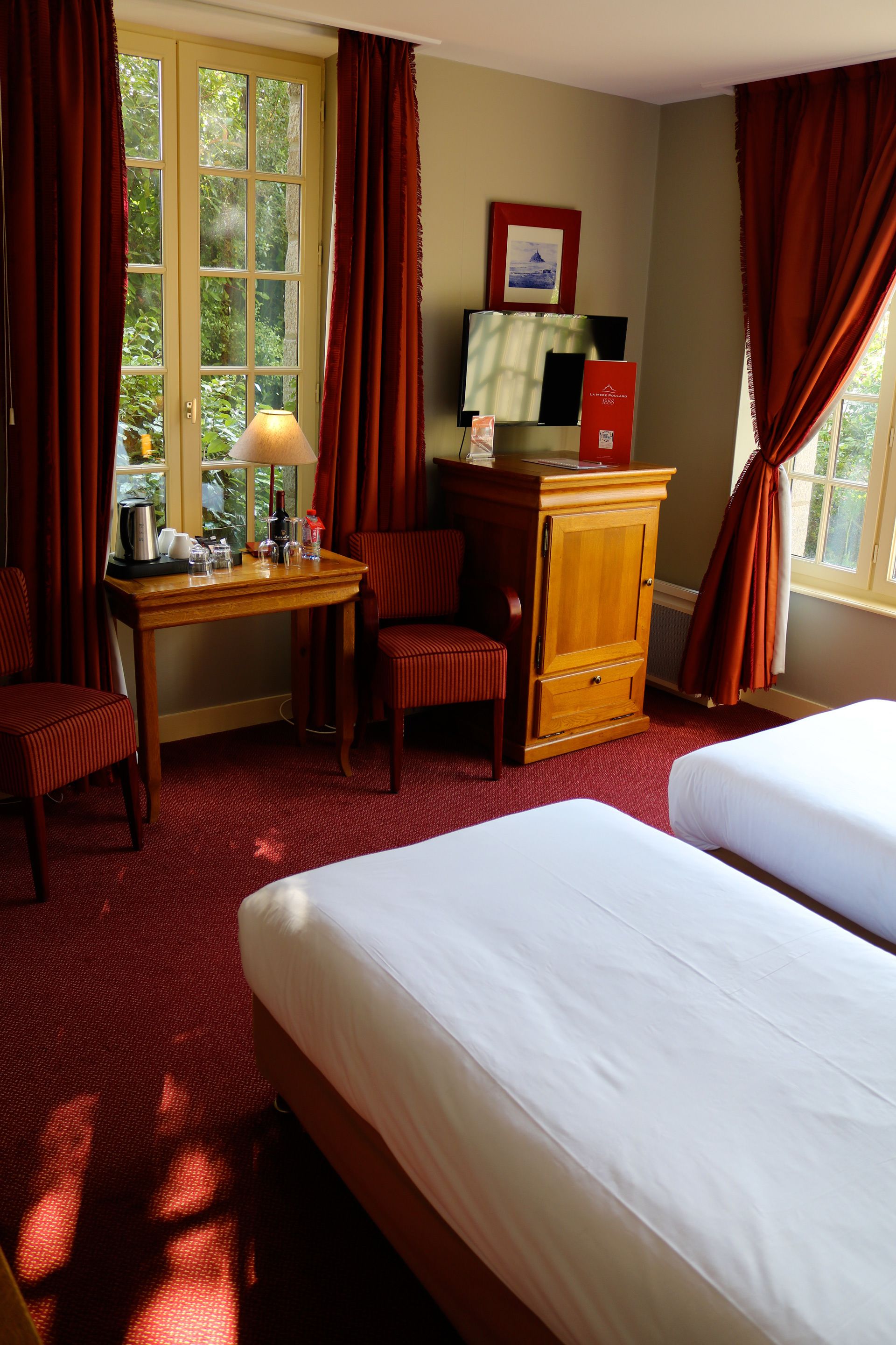 Une chambre d’hôtel avec deux lits, un bureau avec une lampe, une chaise et une armoire.