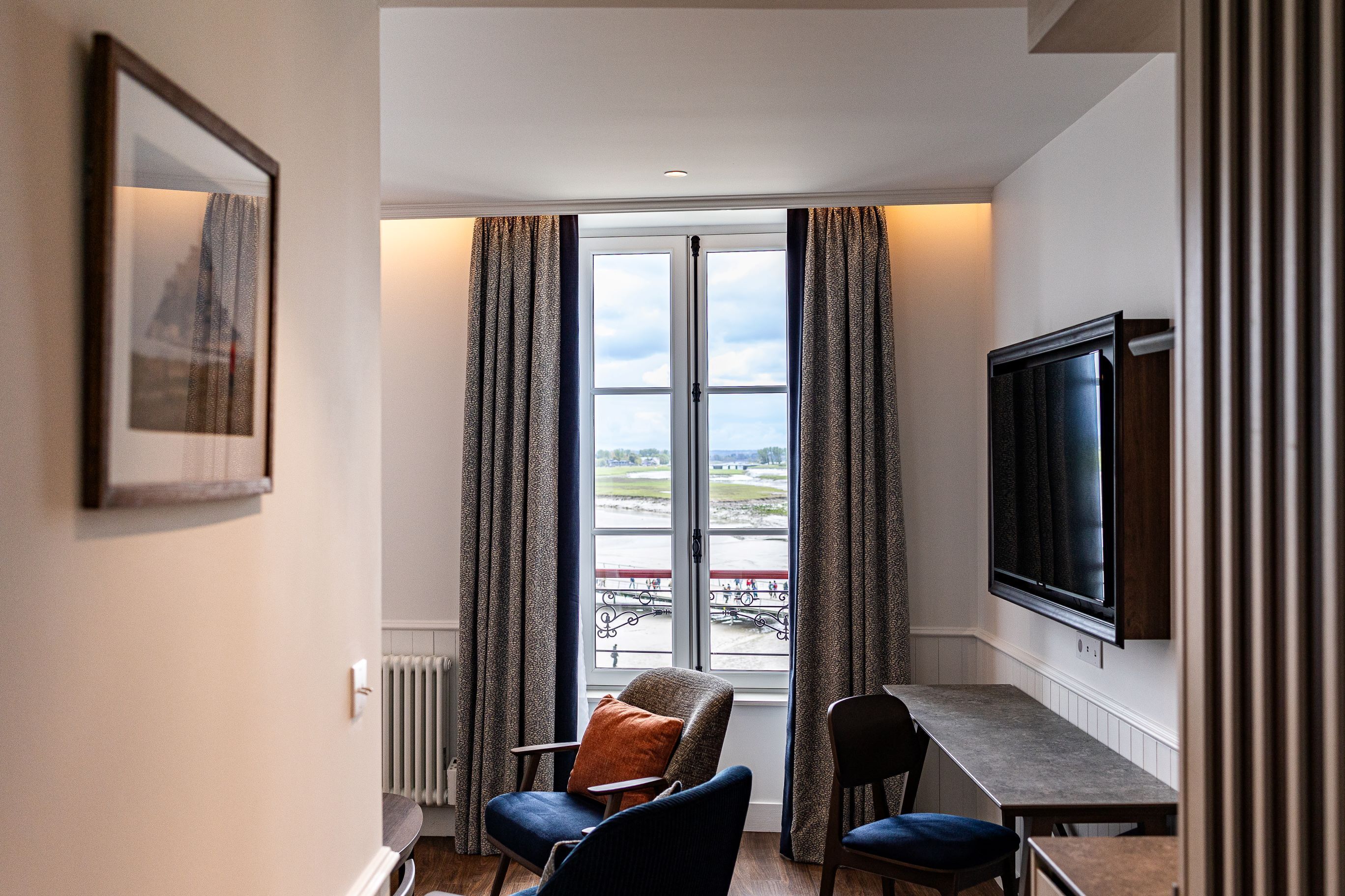A hotel room with a large window, a television, a table, and two chairs.