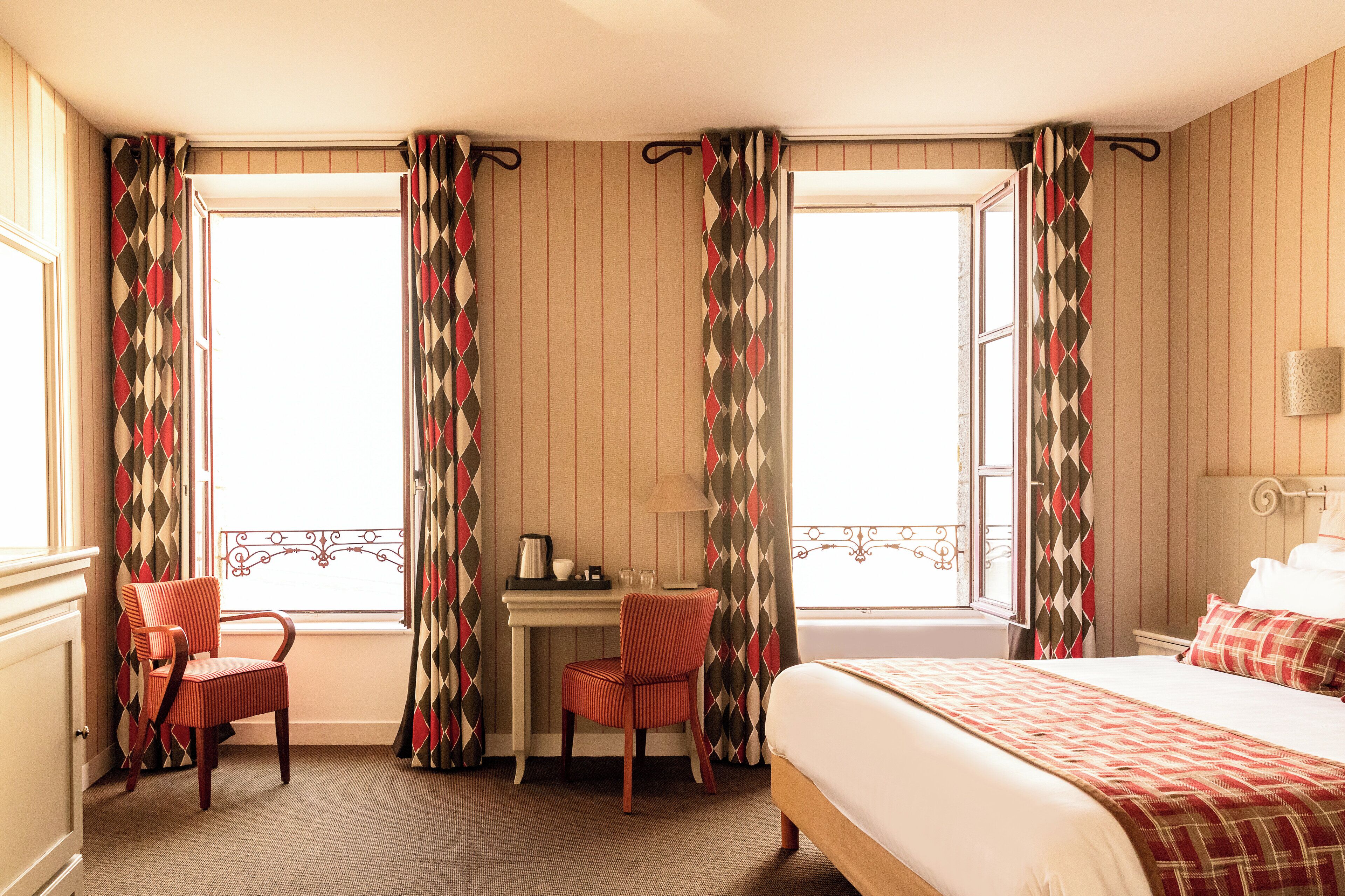 Una habitación de hotel con una cama, un escritorio con una silla y una ventana con cortinas.