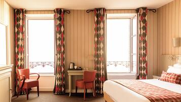 Una habitación de hotel con una cama, un escritorio con una silla y una ventana con cortinas.