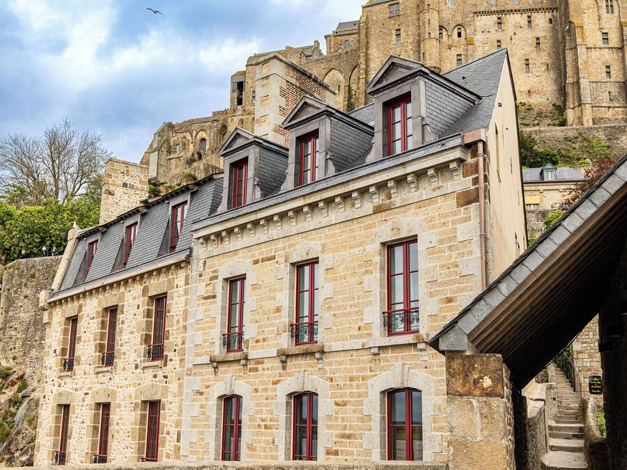 Un edificio de piedra con varias ventanas y balcones, junto a una estructura histórica más grande.