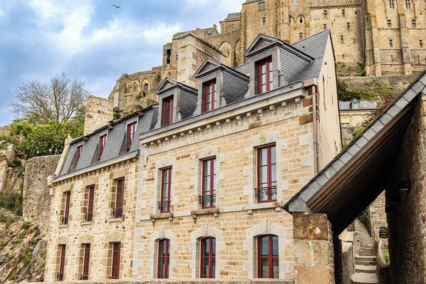 A stone building with multiple windows and balconies, adjacent to a larger historic structure.