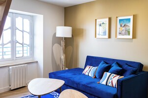 A room with a blue sofa, a white table, and a floor lamp. There are two framed pictures on the wall.
