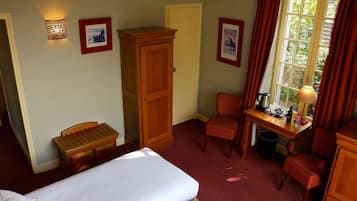 A hotel room with a bed, a desk with a lamp, a chair, a wardrobe, and a window with curtains.