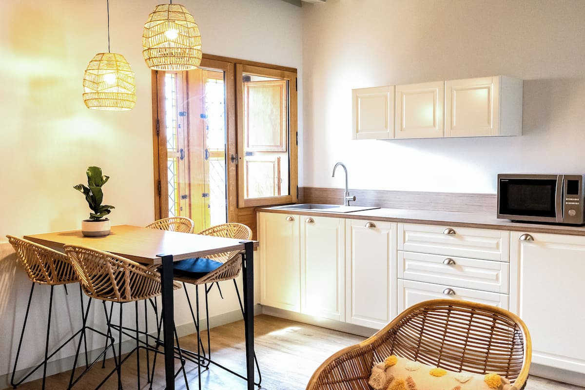 Una cocina con armarios blancos, microondas, sillas de mimbre y una mesa con una planta en maceta.