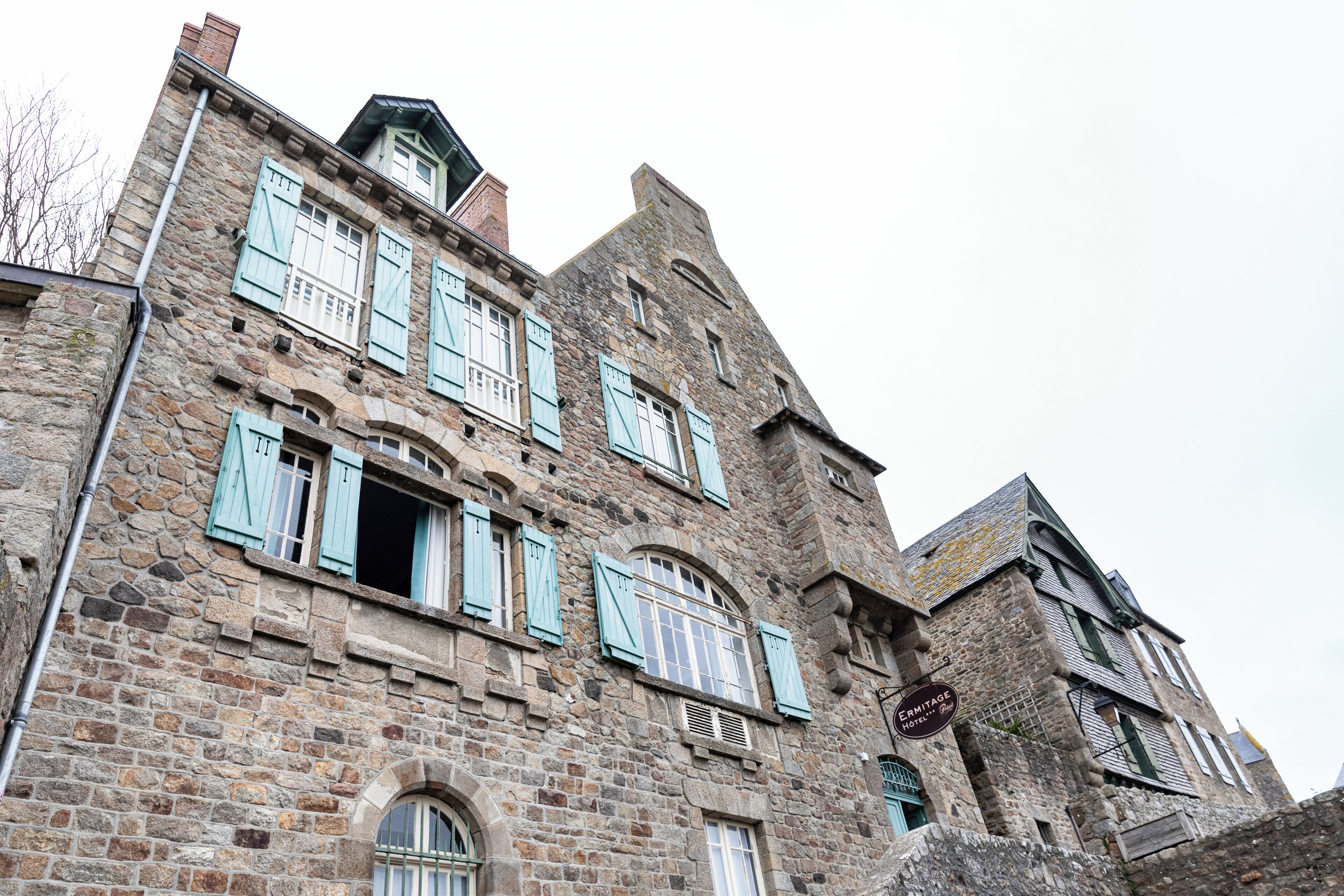 Un edificio histórico de piedra con múltiples ventanas y contraventanas, que destaca por el letrero del Hotel Ermitage.
