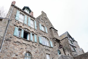 Un edificio histórico de piedra con múltiples ventanas y contraventanas, que destaca por el letrero del Hotel Ermitage.