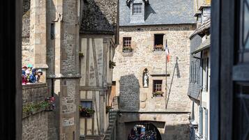 A narrow medieval street with stone buildings, a tower, and a crowd of people.