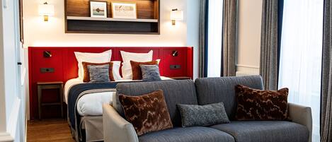 A modern hotel room with a red headboard, a grey sofa, and a wooden side table.