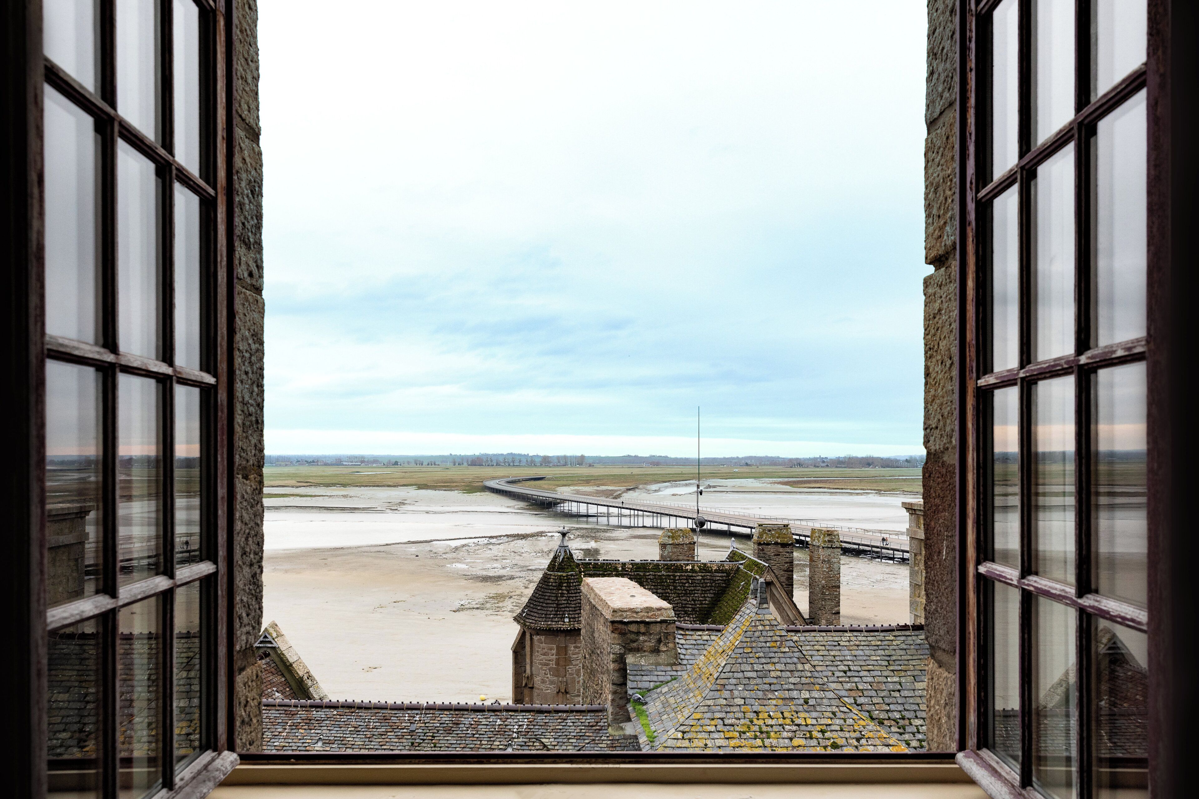 A view from a window overlooking a coastal landscape with a bridge and a stone structure.
