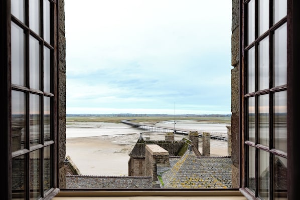 A view from a window overlooking a coastal landscape with a bridge and a stone structure.