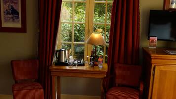 A hotel room with two single beds, a wooden desk with a lamp, a television, and a window with curtains.