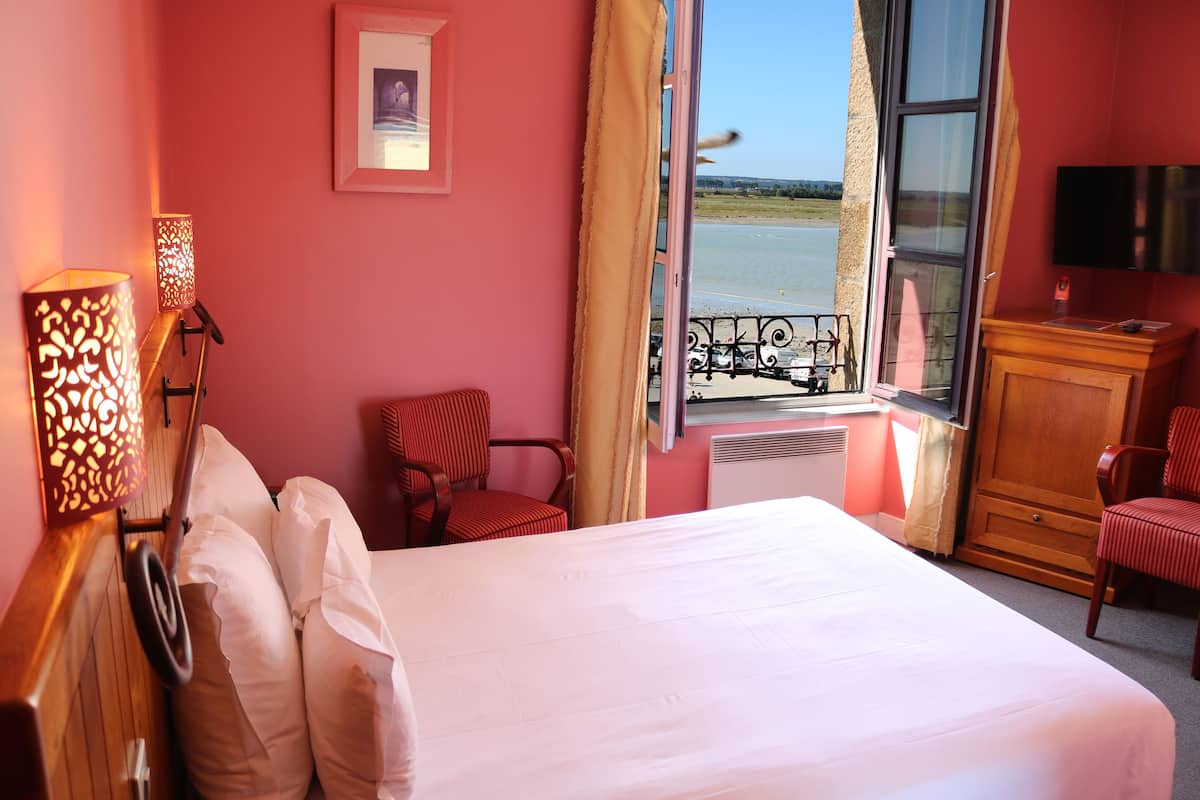 Habitación de hotel con una cama grande, un escritorio, una silla, un televisor y una ventana con vistas al mar.