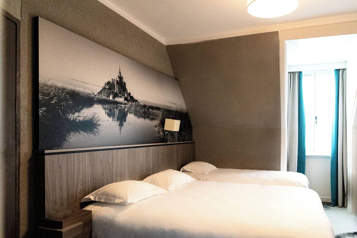 Habitación de hotel con una cama grande, una mesita de noche y un cuadro colgado en la pared que representa un castillo.