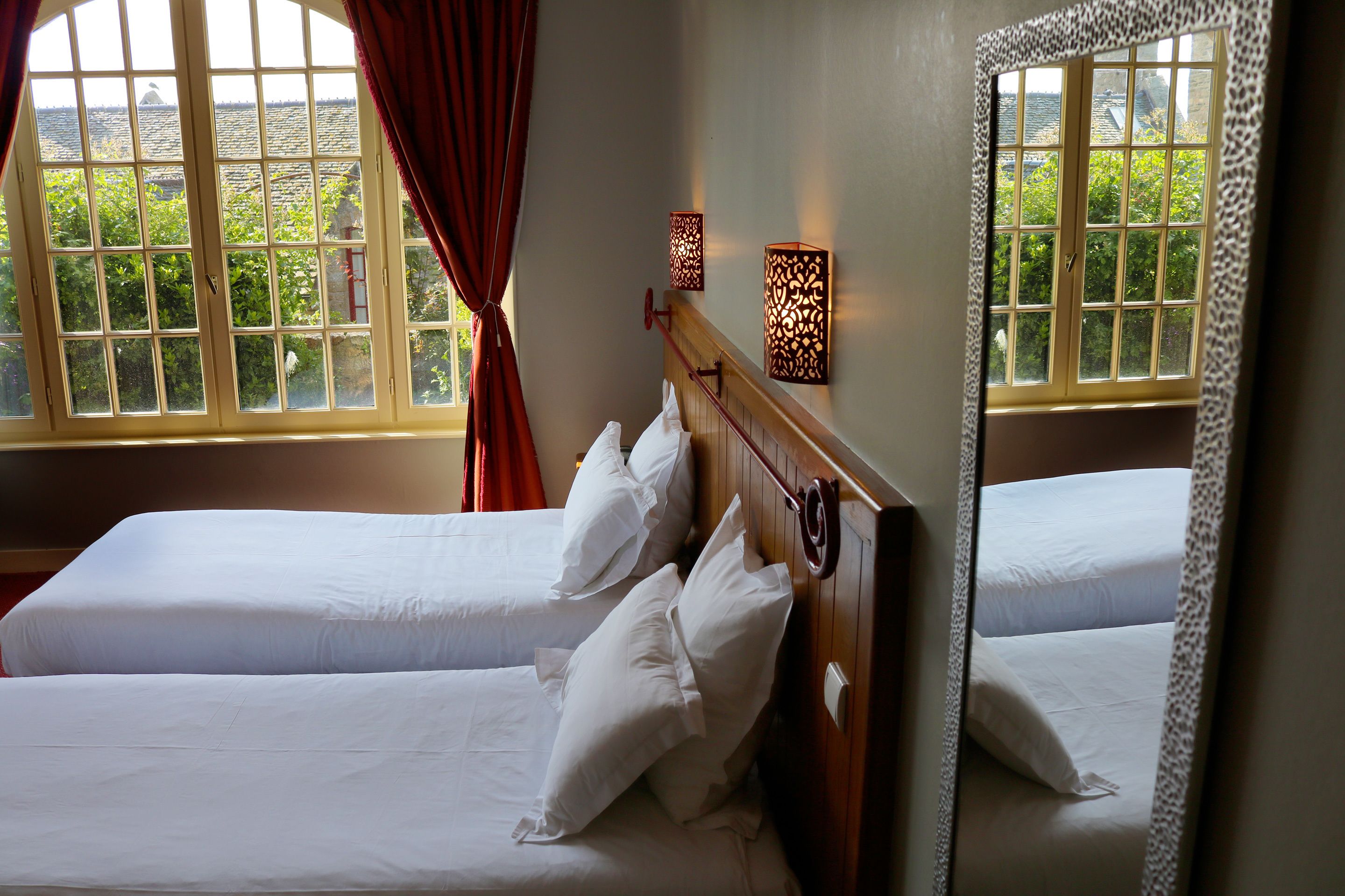 Une chambre d’hôtel avec deux lits, une grande fenêtre avec des rideaux et deux appliques murales.