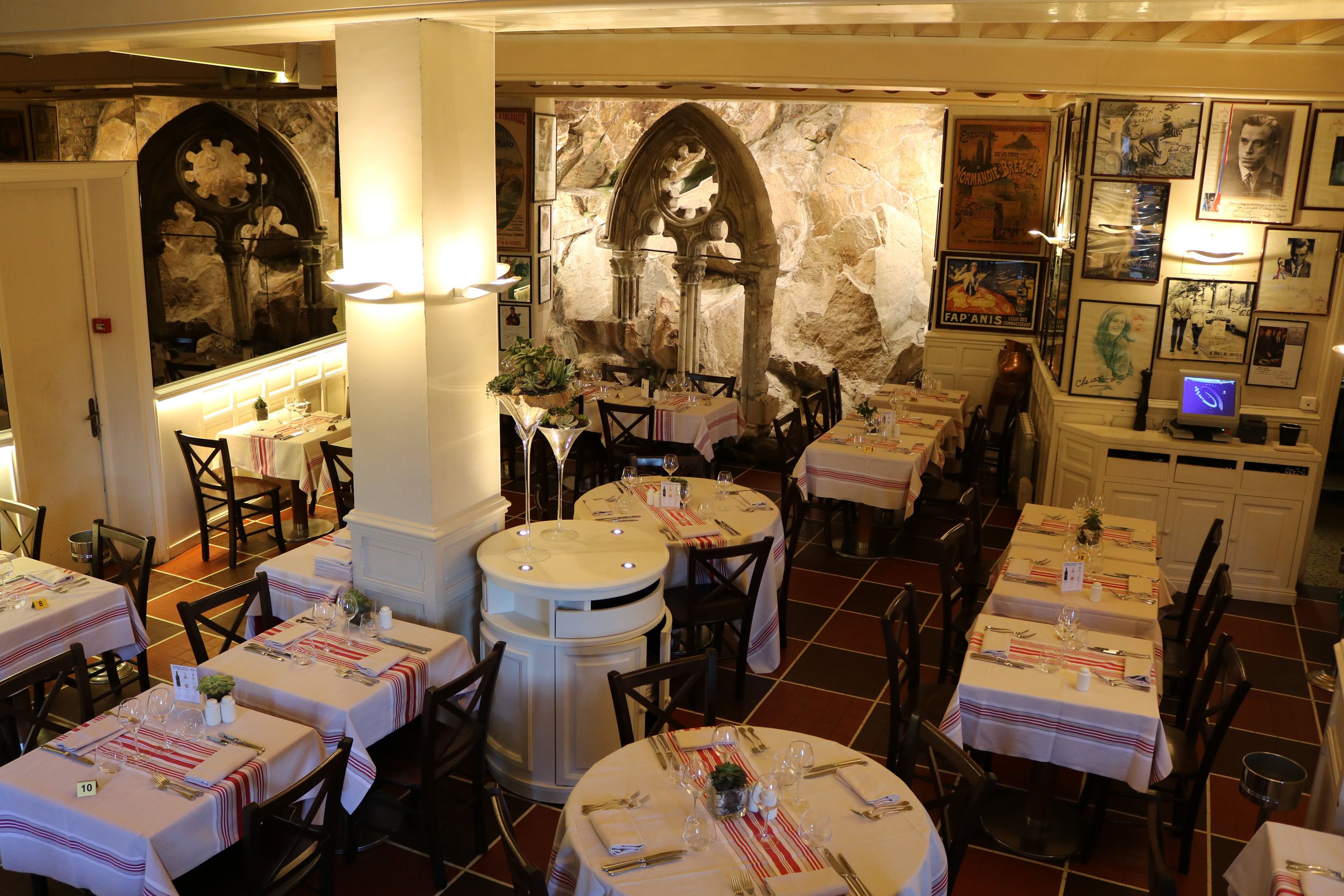 Un restaurant doté de nombreuses tables dressées pour le service, avec un mur en pierre et des tableaux encadrés.