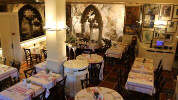 Un restaurant doté de nombreuses tables dressées pour le service, avec un mur en pierre et des tableaux encadrés.