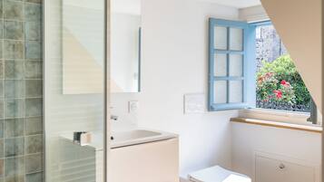 Une salle de bain avec une douche à parois de verre, un lavabo blanc, des toilettes et une fenêtre avec des volets bleus.